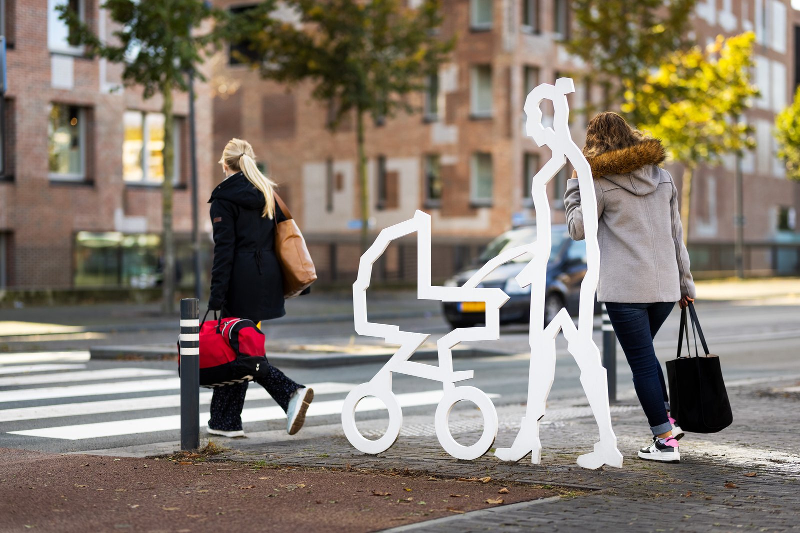 Voetgangers bij een zebrapad naast een attentiefiguur met kinderwagen