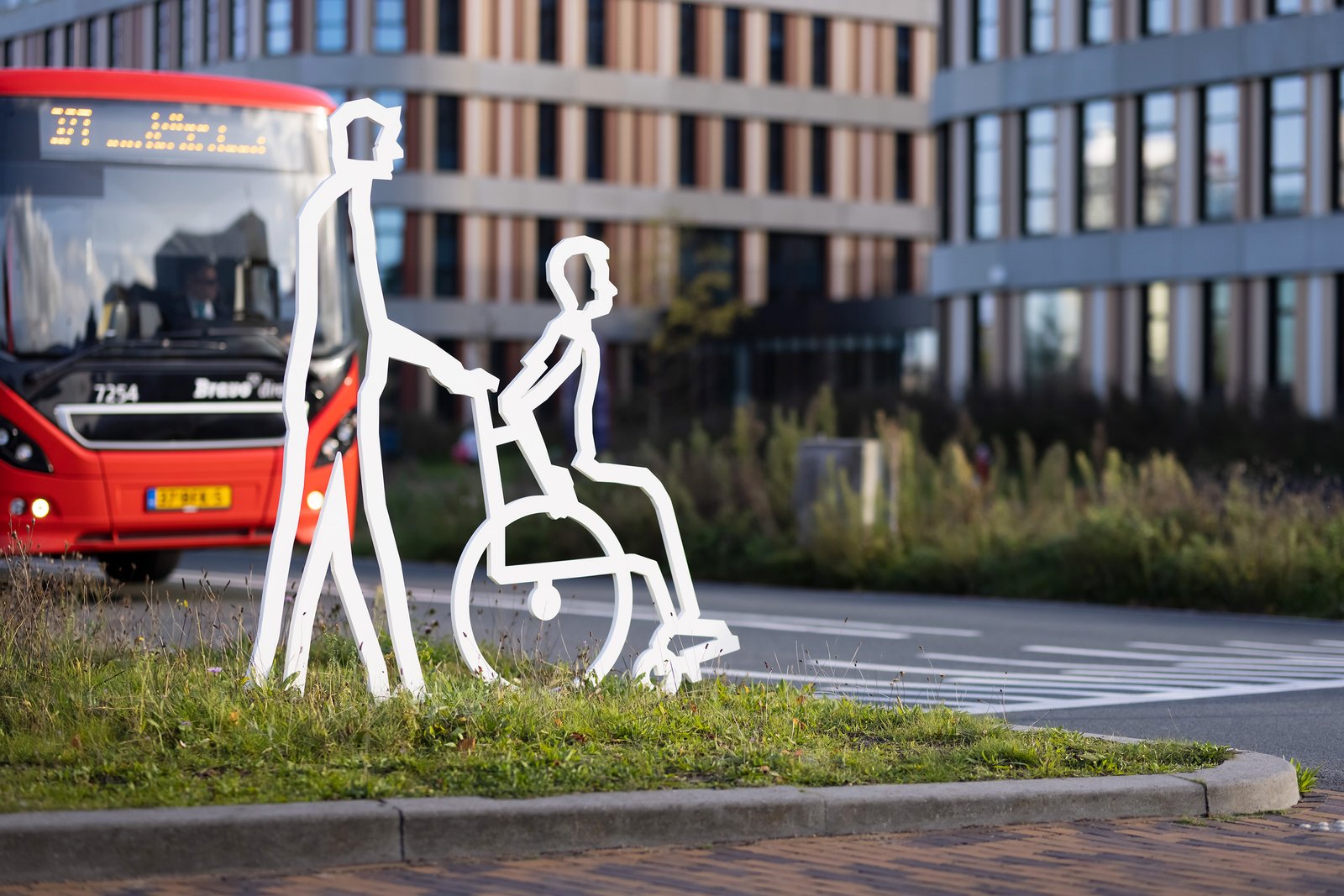 Attentiefiguur begeleider met rolstoelgebruiker bij bushalte