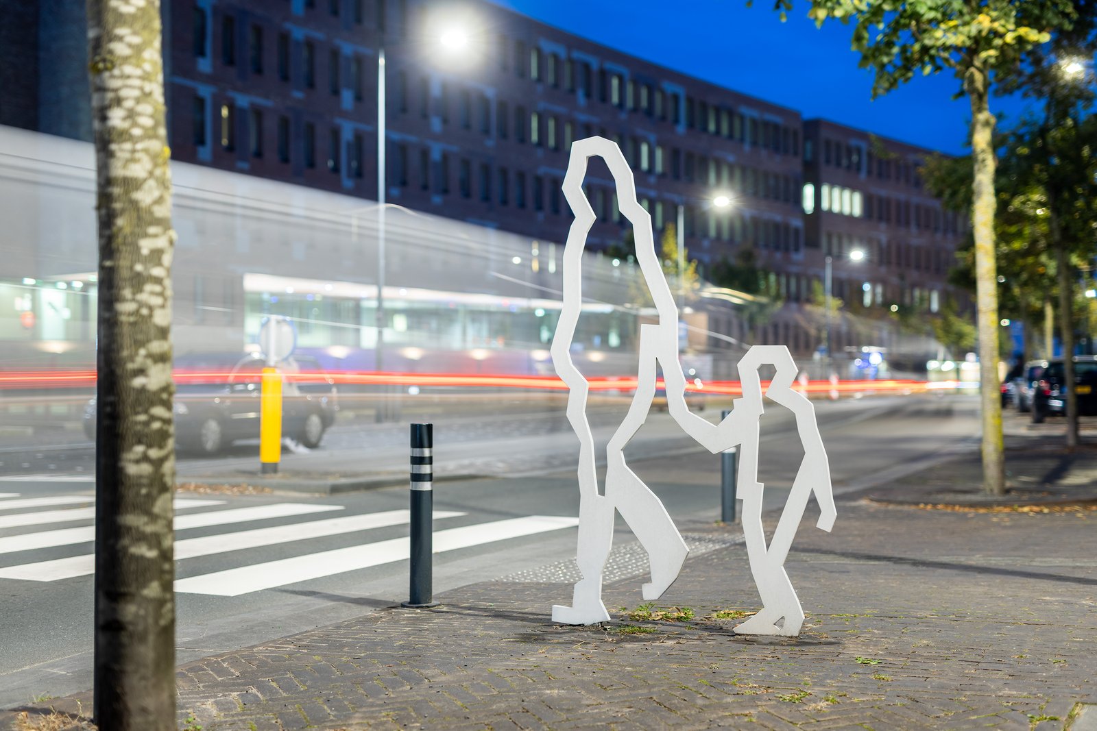Attentiefiguren ouder en kind bij een zebrapad met verkeer in de avond